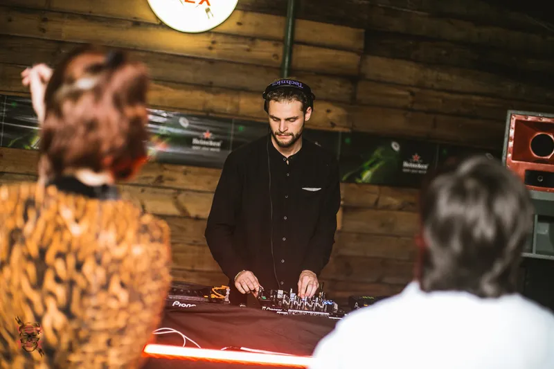 DJ in headphones mixing on Pioneer decks against a wooden wall at a Vortex edition.