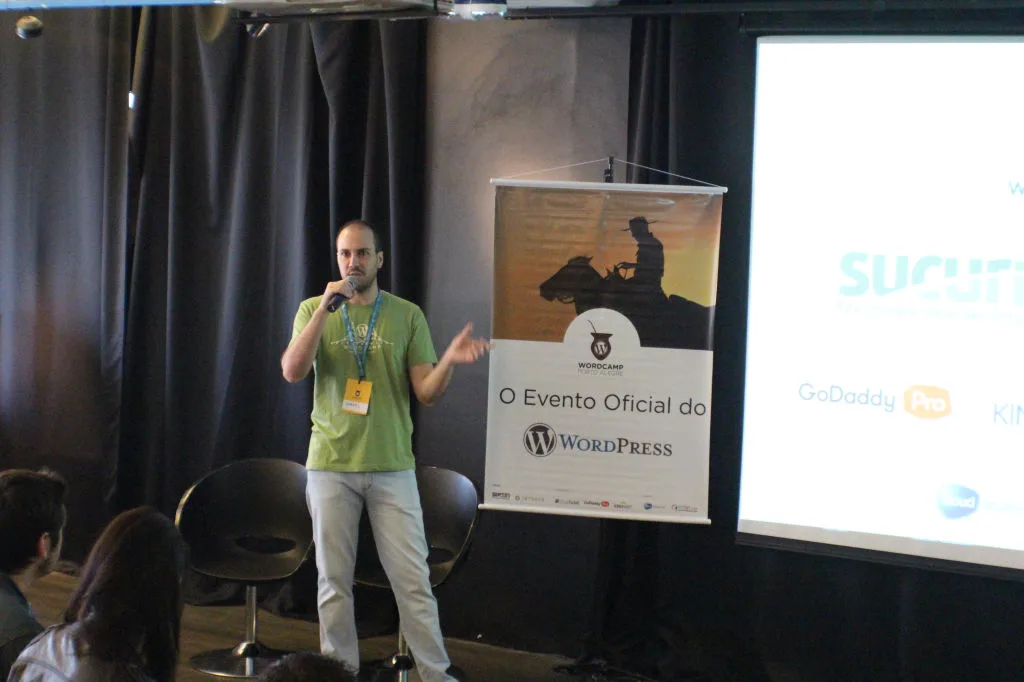 Me on stage at WordCamp Porto Alegre 2015, next to the event banner reading 'O Evento Oficial do WordPress'.